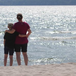 Christina und Carl stehen mit dem Rücken zur Kamera am Strand und blicken aufs Wasser.