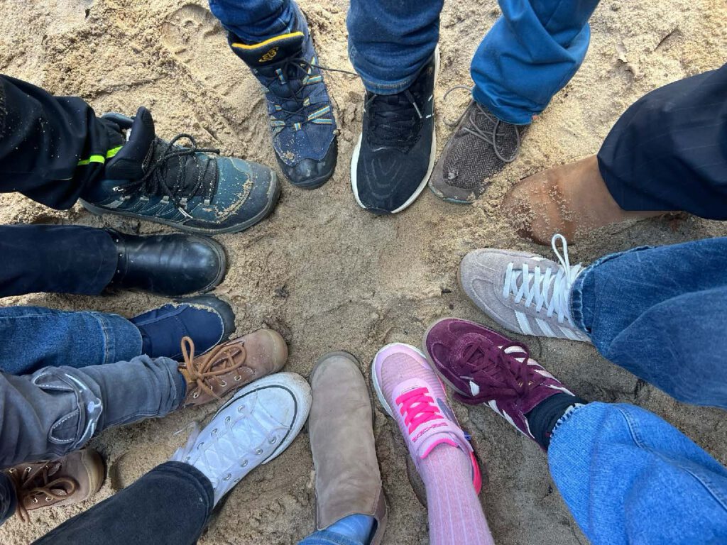 Die Füße von 13 Kindern stehen im Kreis in einem Sandkasten.